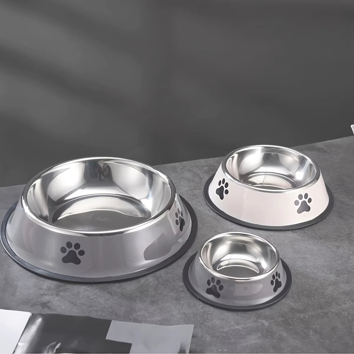 Three grey stainless steel dog bowls in different sizes on a stone surface